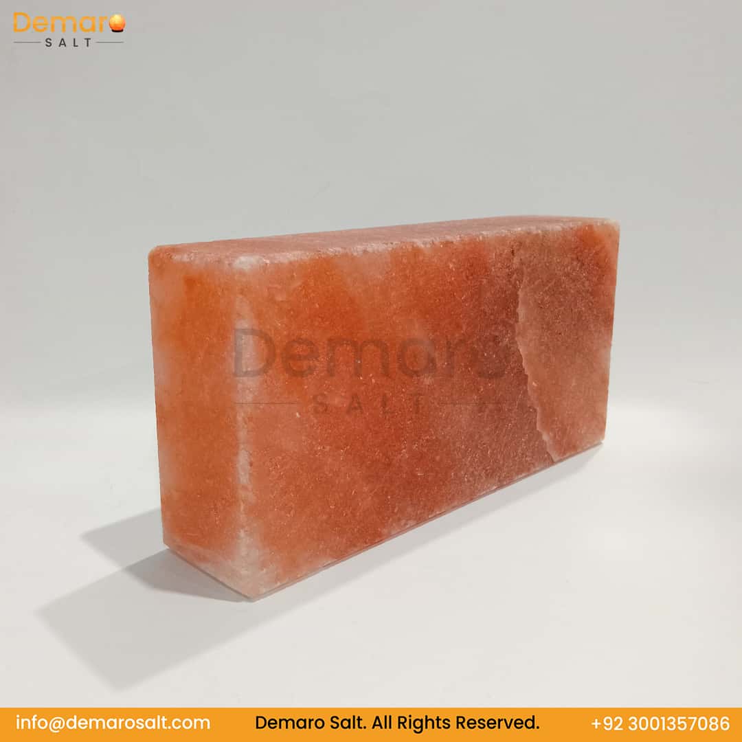 A rectangular block of pink Himalayan salt, resting on a white surface with a gray background. The logo "Demaro Salt" is visible in the top left and watermarked in the center. Contact information is at the bottom of the image.