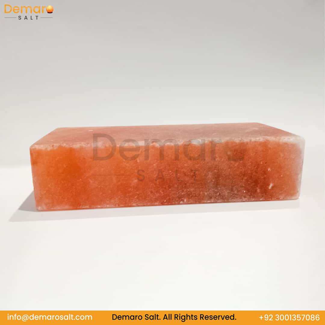 A rectangular block of pink Himalayan salt, resting on a white surface with a gray background. The logo "Demaro Salt" is visible in the top left and watermarked in the center. Contact information is at the bottom of the image.