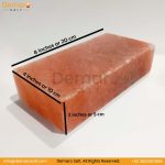 A rectangular block of pink Himalayan salt, resting on a white surface with a gray background. The logo "Demaro Salt" is visible in the top left and watermarked in the center. Contact information is at the bottom of the image.
