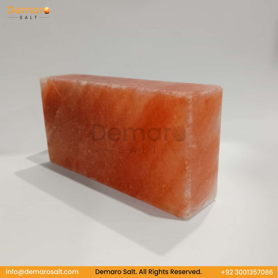 A rectangular block of pink Himalayan salt, resting on a white surface with a gray background. The logo "Demaro Salt" is visible in the top left and watermarked in the center. Contact information is at the bottom of the image.