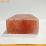 A rectangular block of pink Himalayan salt, resting on a white surface with a gray background. The logo "Demaro Salt" is visible in the top left and watermarked in the center. Contact information is at the bottom of the image.