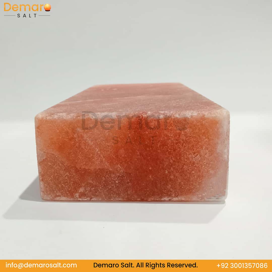 A rectangular block of pink Himalayan salt, resting on a white surface with a gray background. The logo "Demaro Salt" is visible in the top left and watermarked in the center. Contact information is at the bottom of the image.